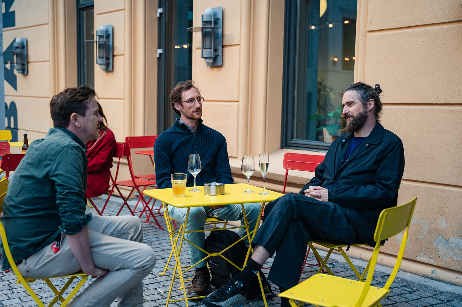 Three participants talking at a yellow table in the courtyard
